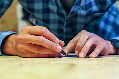 Nahaufnahme: Hände zeichnen mit einem Stift auf einem Blech an