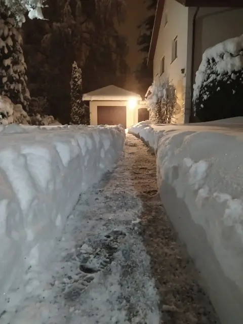 Nachts frei geräumter Weg zwischen hohen Schneewänden vor einer Garage