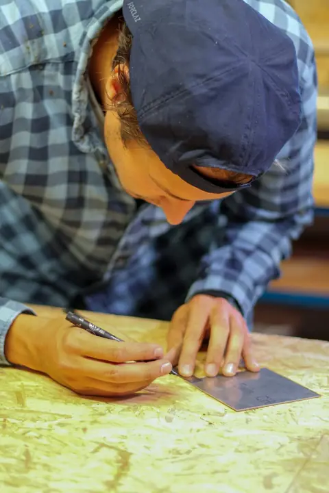 Victor zeichnet in der Werkstatt ein Blechschild an